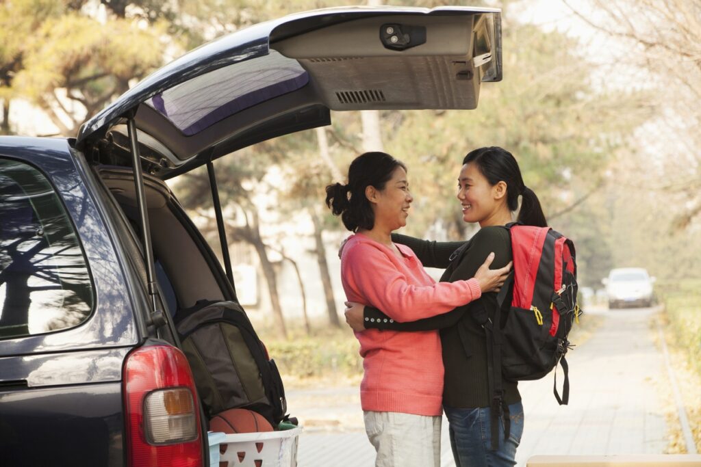 Mother and daughter embracing behind car on college move in day
